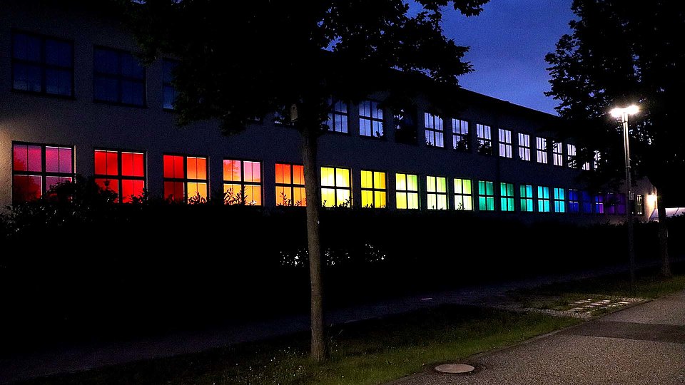 Outside of the Ferdinand-Braun-Institut at night with colorfully illuminated windows.