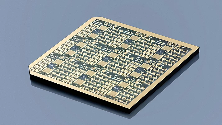 Wafer auf einem grauen Hintergrund. Die obere Fläche zeigt ein komplexes Muster aus kleinen quadratischen und rechteckigen Strukturen, die verschiedene Leiterbahnen und elektrische Verbindungen repräsentieren.