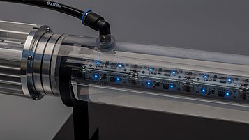 Transparent cylinder with built-in blue LED lights and electronic components. A connecting element can be seen at one end of the cylinder.