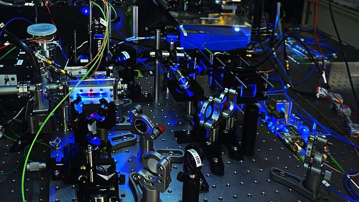 Experimental apparatus with various optical components, metal supports and colorful cables. The structure is illuminated by blue and green lights.