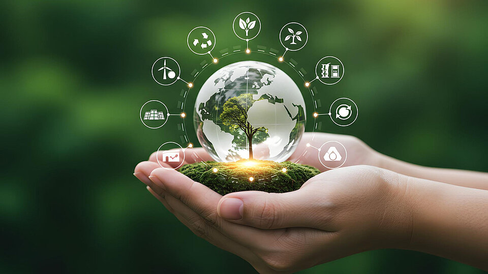Eine Hand hält eine gläserne Kugel mit einem Baum und einer Weltkarte, umgeben von Symbolen für Umweltschutz, erneuerbare Energien und nachhaltige Entwicklung.
