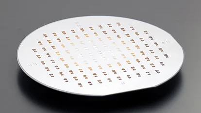 Round semiconductor wafer viewed at an angle, patterned with evenly spaced small square and circular cells in rows across its surface.