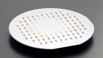 Round semiconductor wafer viewed at an angle, patterned with evenly spaced small square and circular cells in rows across its surface.