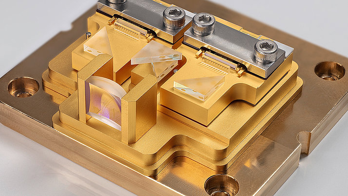 Pumplasermodul aus goldfarbenem Material mit mehreren prismatischen Elementen. Die Struktur zeigt eine Kombination von eckigen und runden Formen, die zur Manipulation von Lichtstrahlen verwendet werden. 