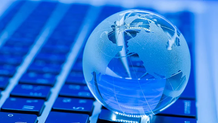 Eine transparente Weltkugel auf einer Laptop-Tastatur, vor blauem Hintergrund.
