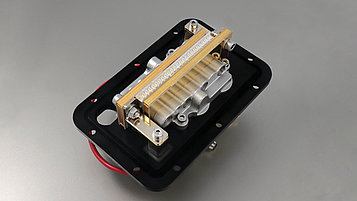 A mechanical component on a black background, with a silver housing and a gold strip. The part contains various moving elements and connections.