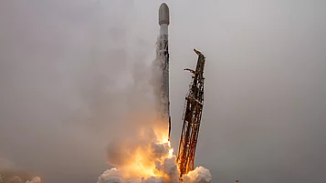 A rocket launches from a launch pad as flames and smoke pour from its engines. The sky is cloudy, and the scene conveys a sense of movement and energy.