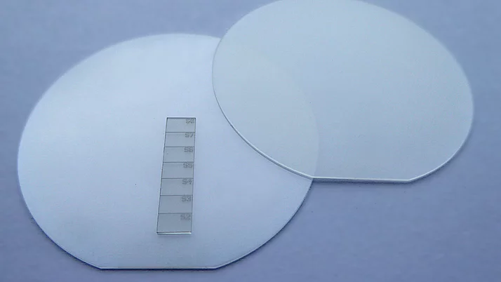 Two transparent, round wafers lie next to each other on a surface. Next to them is a thin glass scale with test lines numbered from S2 to S7. 