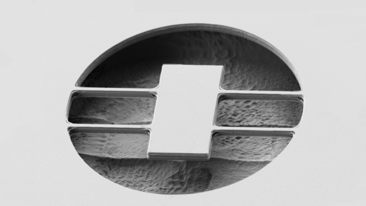 Microscopic image of a DBR mirror layer with a central, cross-striped structure. The surface shows fine textures and details that are visible under high magnification