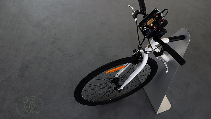 A modern bike with a control element on the handlebars. The bike has a white frame and is held by a sturdy, gray stand.