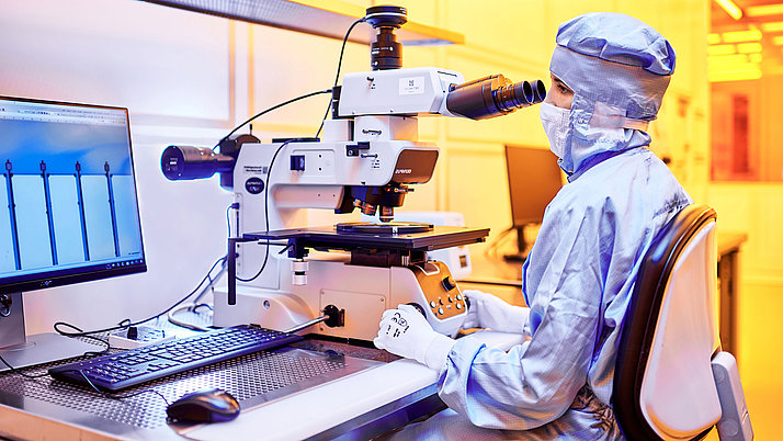 Female employee in a clean room suit working on a microscope