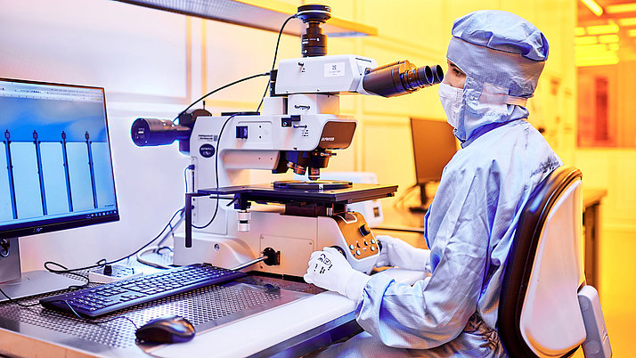 Female employee in a clean room suit working on a microscope