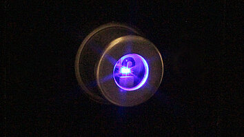 Close-up of an InGaN-based laser diode emitting blue-violet light, captured in a dark environment.