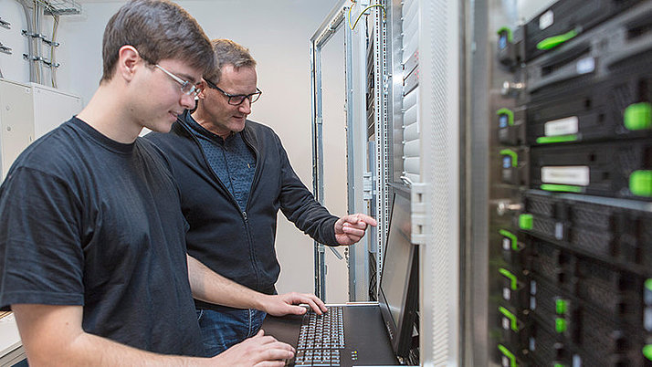 Zwei Fachinformatiker stehen vor einem Rechner in einem Serverraum.
