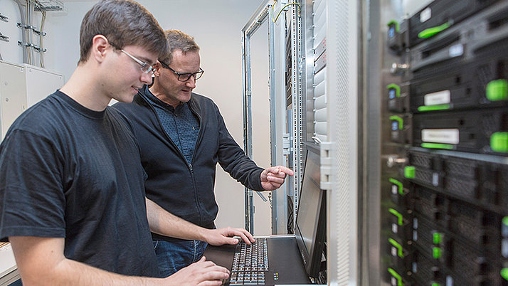 Zwei Fachinformatiker stehen vor einem Rechner in einem Serverraum.