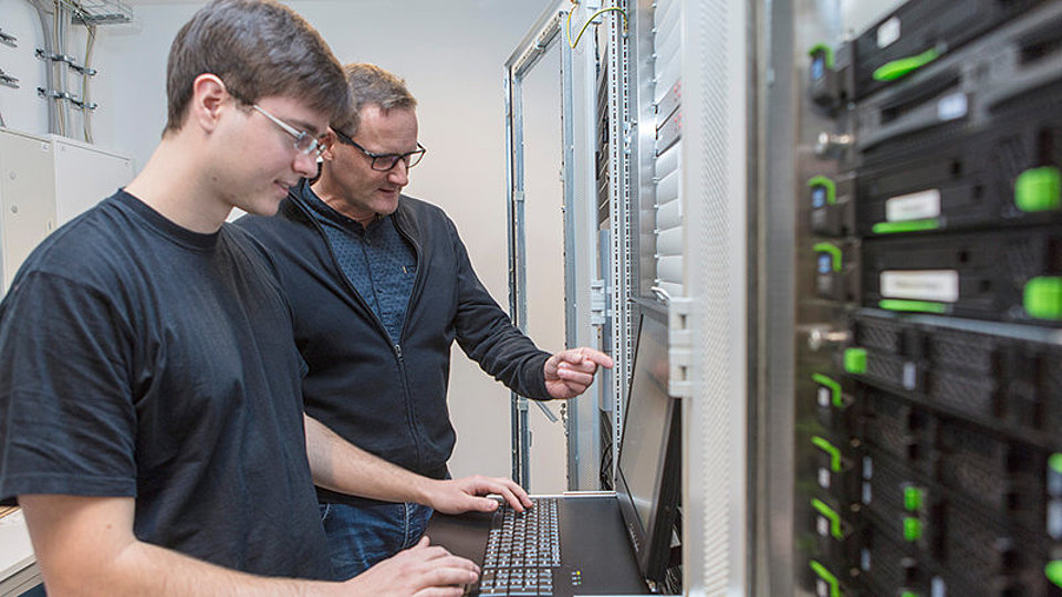 Two IT specialists standing in front of a computer in a server room.