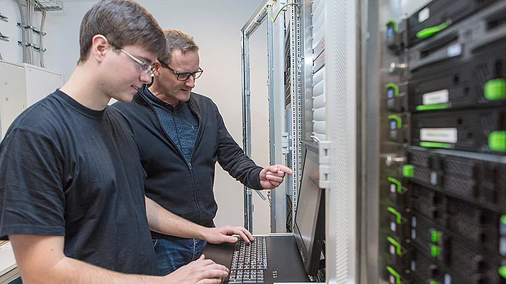 Zwei Fachinformatiker stehen vor einem Rechner in einem Serverraum.