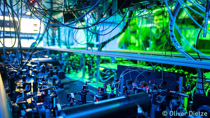 Komplexe Anordnung von optischen Instrumenten und Kabeln in einer Laborumgebung. Grünes und blaues Licht beleuchtet die Szene.