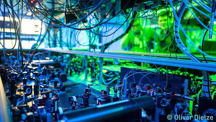 Komplexe Anordnung von optischen Instrumenten und Kabeln in einer Laborumgebung. Grünes und blaues Licht beleuchtet die Szene.