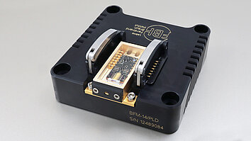 The image shows a laser module in a butterfly housing integrated into a black fixture. It bears the inscription “BFM-14/PLD” and a serial number. The lower part has gold contacts that are used to connect to other devices.