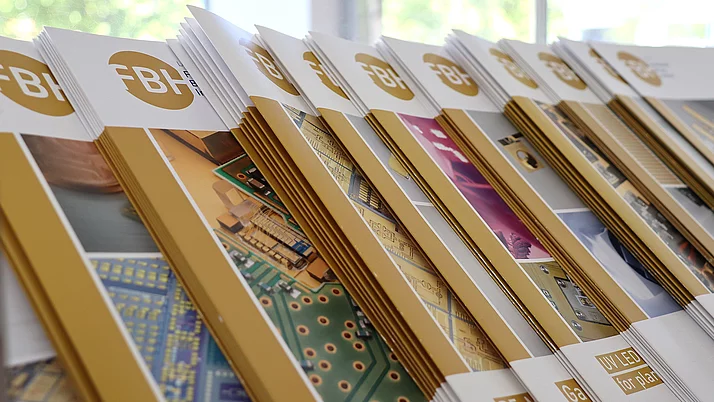 Eine Reihe von Informationsbroschüren mit dem Logo "FBH" sind auf einem Tisch angeordnet. Die Broschüren zeigen technische Illustrationen und Grafiken zum Thema LED-Technologie und elektronische Schaltungen.