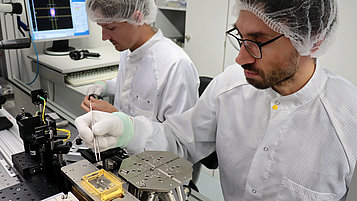 The photo shows two employees working on a diode laser module in a laboratory.