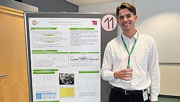 Ein junger Mann in einem weißen Hemd steht lächelnd neben einem wissenschaftlichen Poster und hält ein Glas in der Hand. Das Poster zeigt Forschung zu einem Pikosekunden-Pulsgenerator mit InP-HBTs.