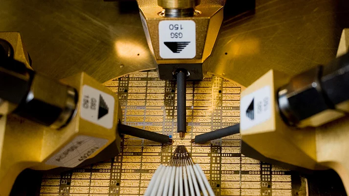 Close-up of an automated production machine that processes semiconductor wafers. The machine uses several pointed contacts to make precise connections on the surface of the wafer.