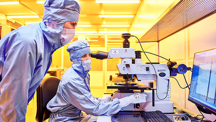 Zwei Frauen im Reinraum des FBH, die eine Waferstruktur auf einem Monitor betrachten