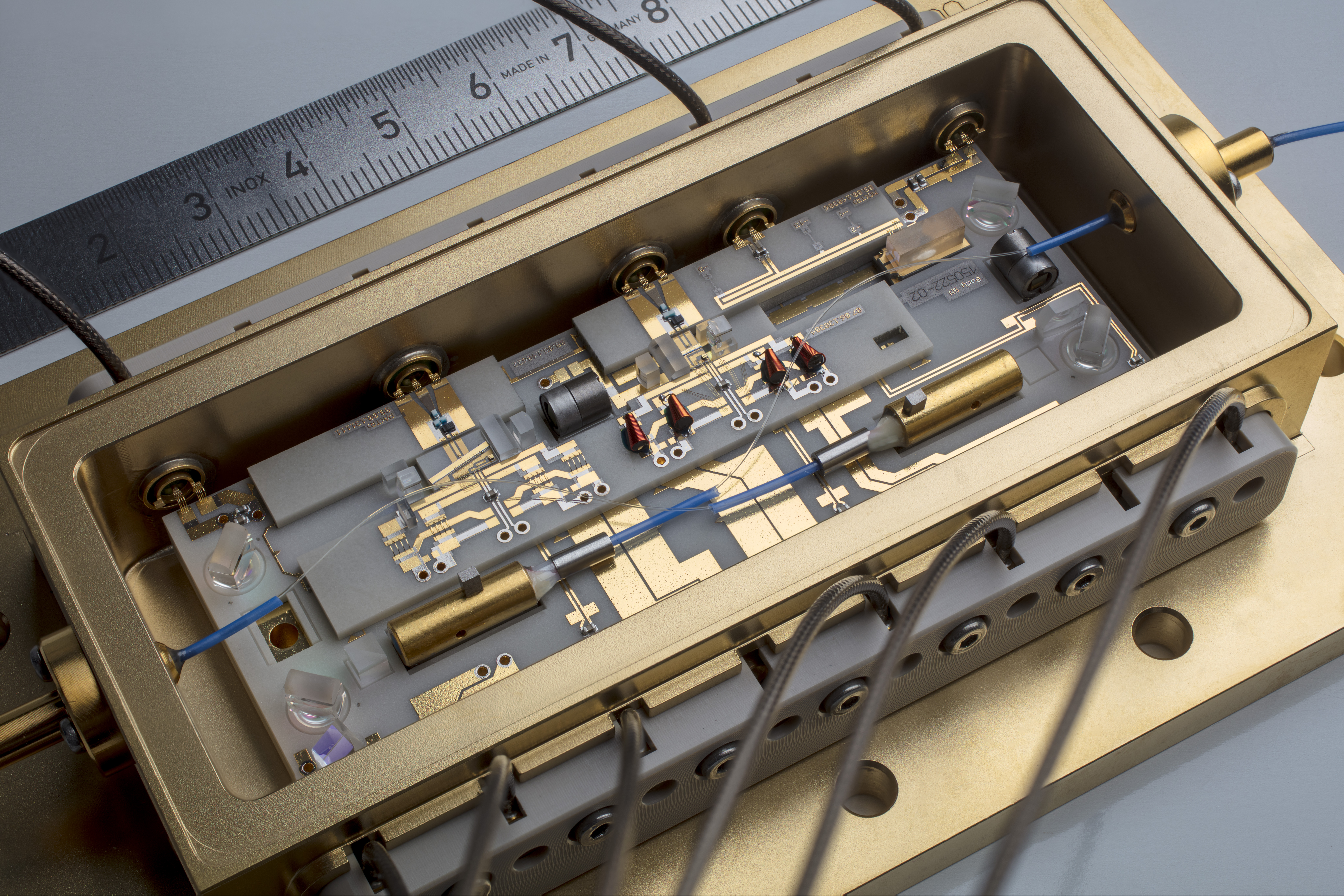 Complex electronic circuit in a gold-colored housing. Various components such as resistors, transistors and connecting wires are visible. A ruler is placed next to it.